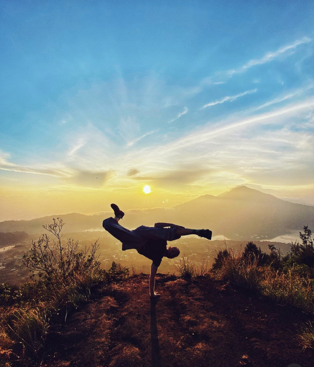 Silhouette of hikers reaching the summit of Mount Batur at sunrise, with glowing sky and volcanic ridges in the background